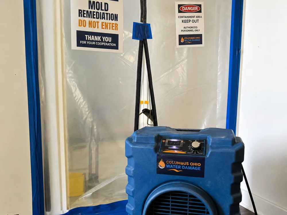 HEPA air scrubber operating inside a taped plastic containment doorway with a sealed zipper entry